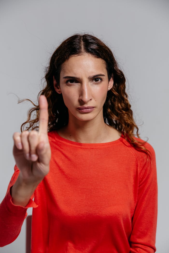 Portrait of a confident woman making an assertive gesture in a studio setting, wearing a red shirt.